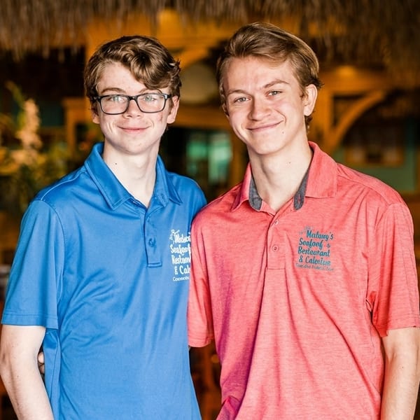 Two young men in blue and red Matlacha's Seafood Restaurant & Catering polo shirts smile.