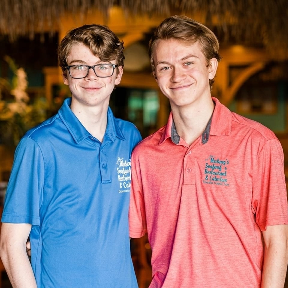 Two young men in blue and red Matlacha's Seafood Restaurant & Catering polo shirts smile.