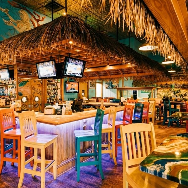 A vibrant restaurant interior with a tiki bar, colorful stools, and tropical decor.