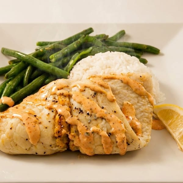 Grilled chicken with sauce, white rice, green beans, and a lemon wedge on a white plate.